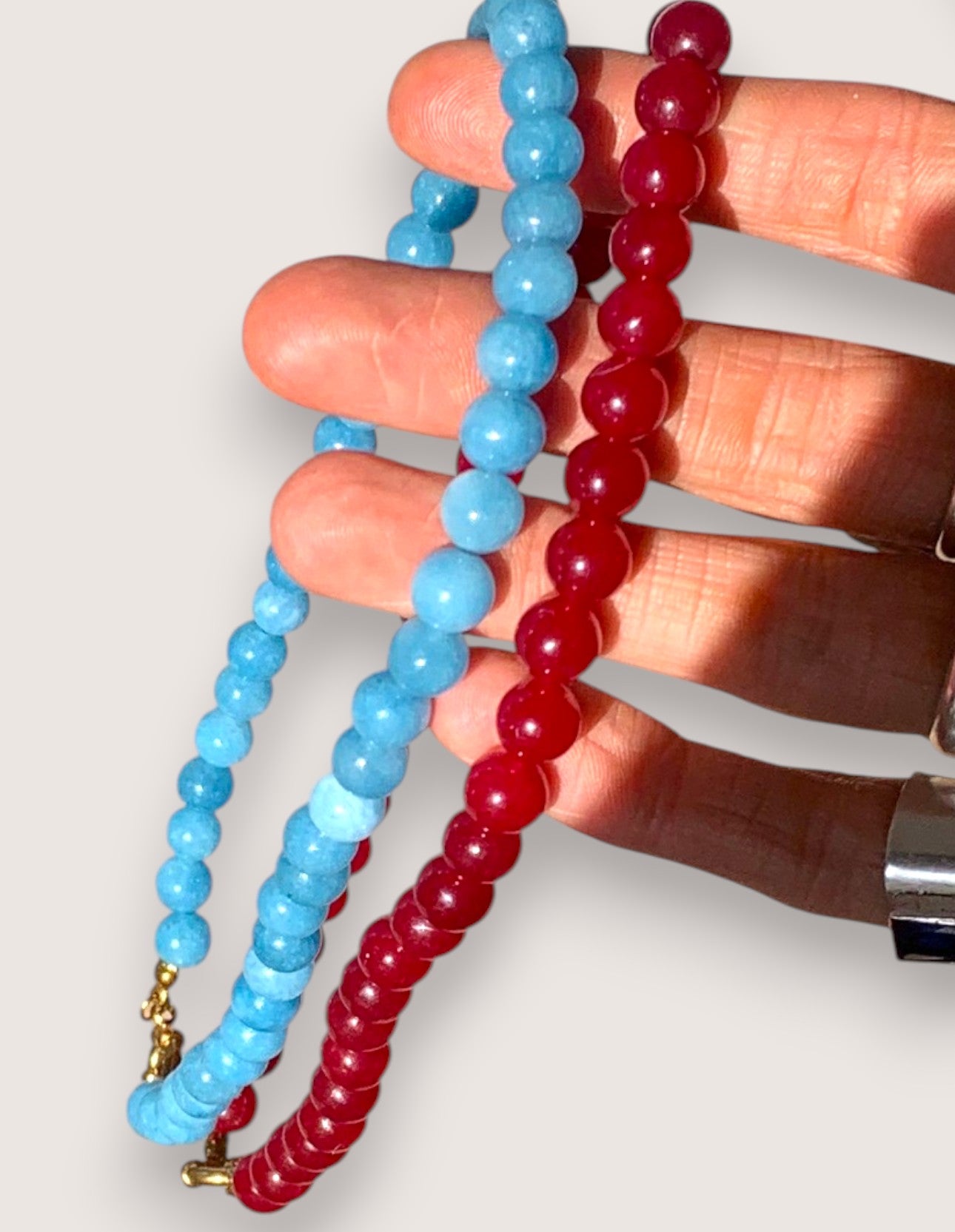 Hand holding two beaded bracelets, one blue and one red, on a light background