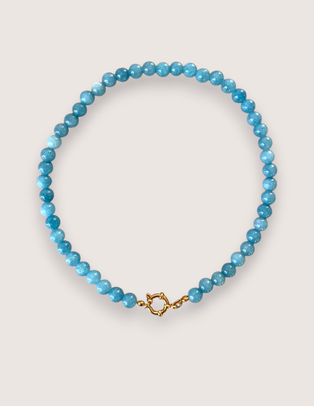 Blue beaded necklace with a gold clasp on a light gray background