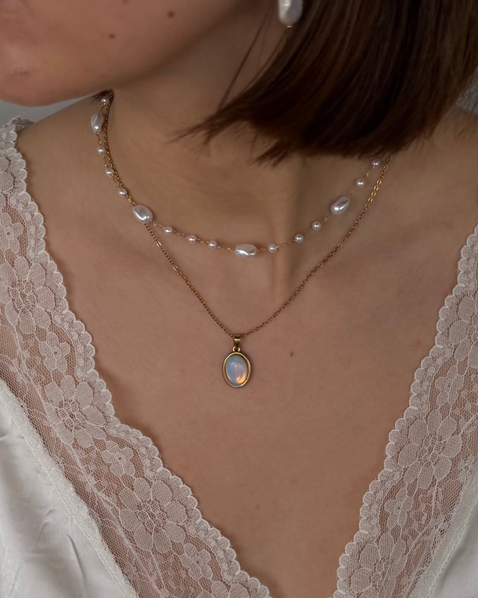 Close-up of a person wearing a delicate necklace with a pendant and pearl necklace.
