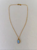 Gold necklace with a blue gemstone pendant on a white background