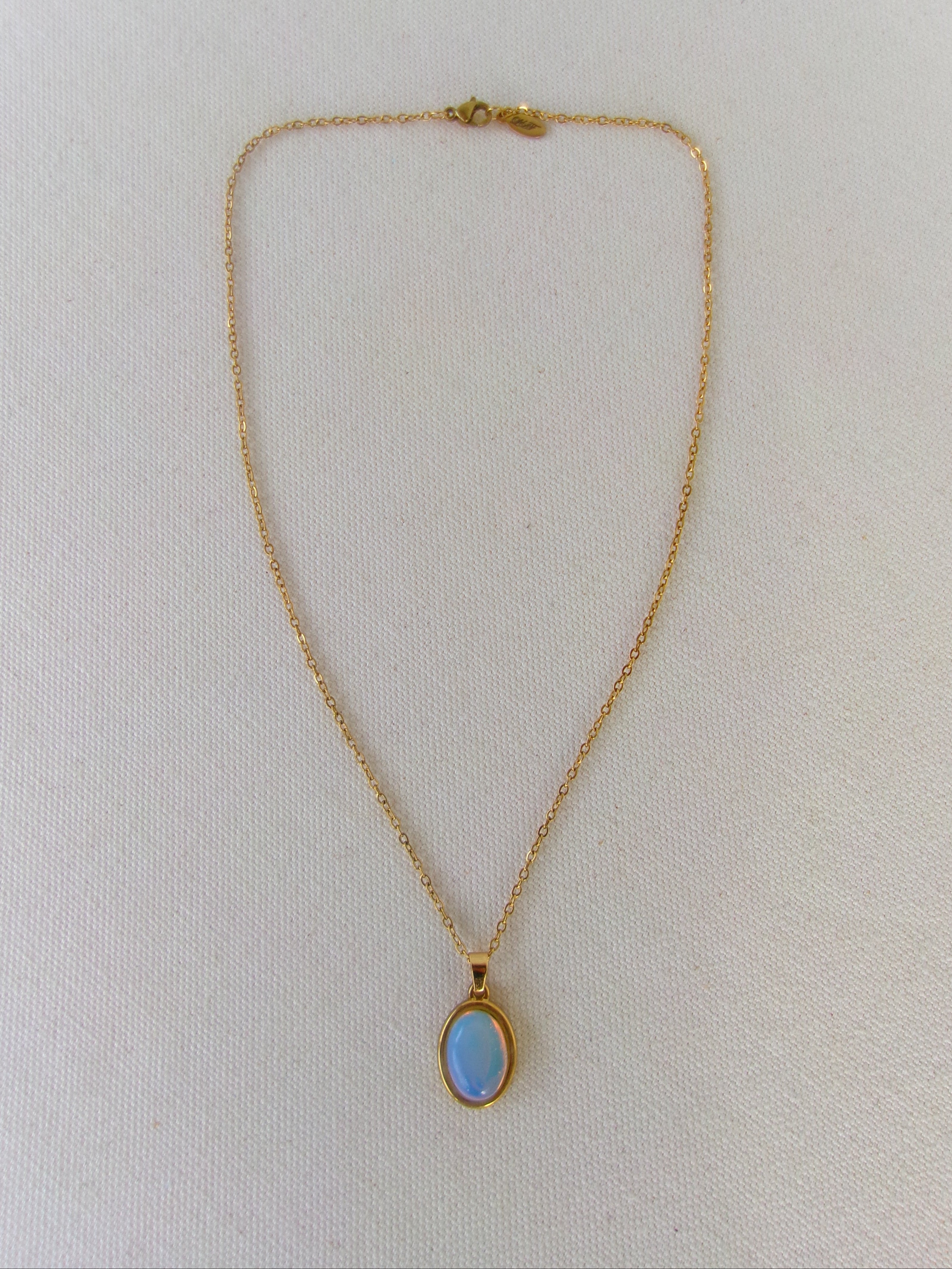 Gold necklace with a blue gemstone pendant on a white background