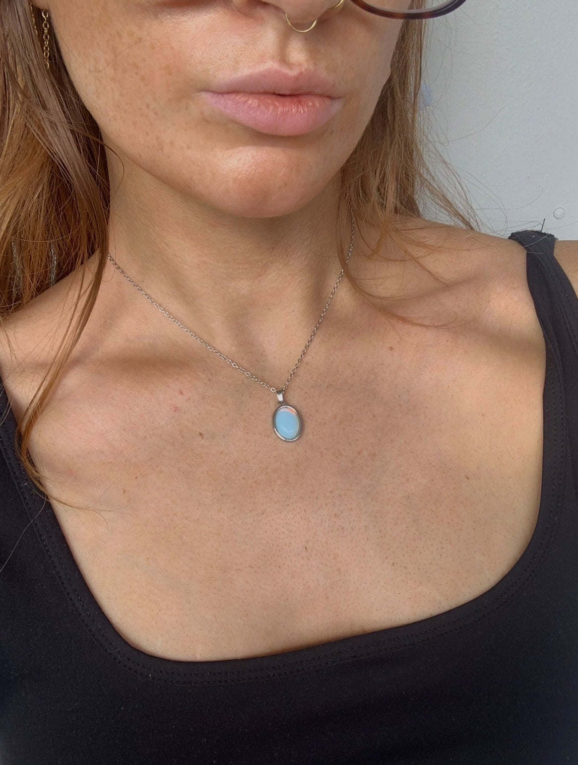 Woman wearing a black top with a necklace featuring a blue pendant against a neutral background