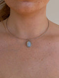 A close-up of a person's neck and chest wearing a delicate silver wire choker necklace with a small oval light blue-gray pendant.