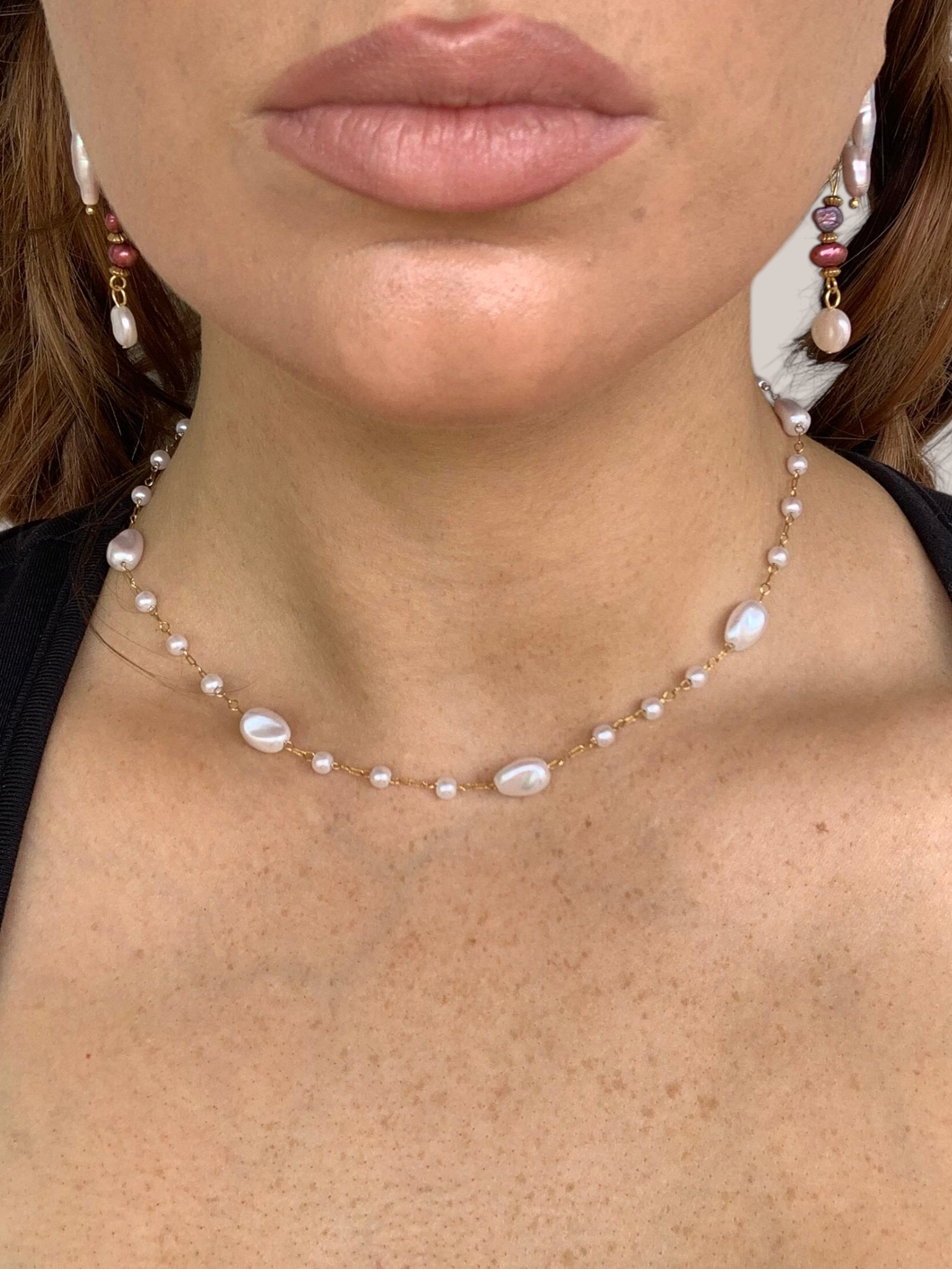 Close-up of a woman wearing a pearl necklace and earrings against a neutral background