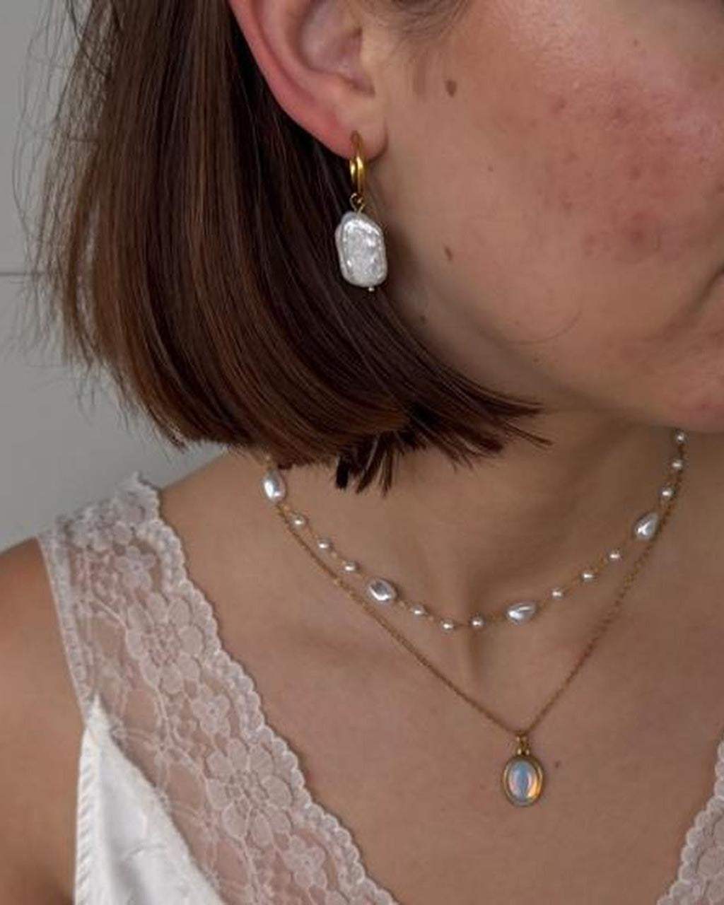 woman wearing pearl hoop gold earrings and layered handmade necklaces