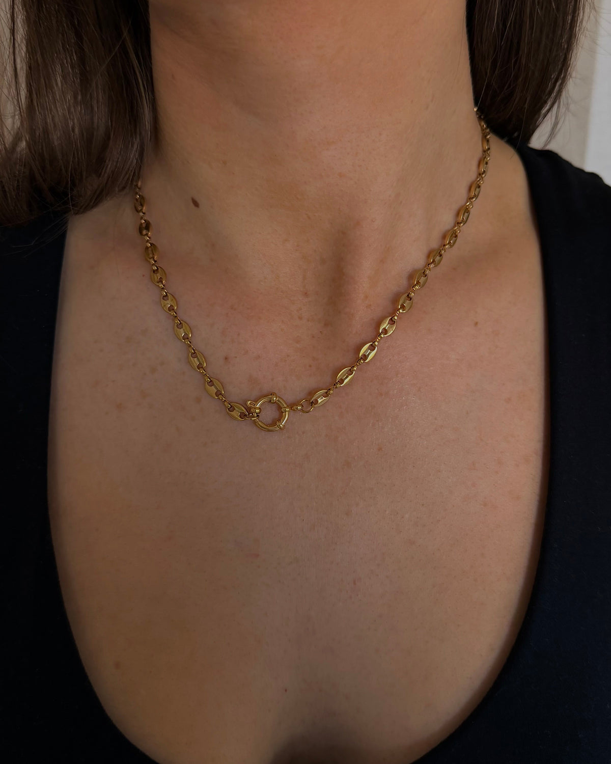 A close-up of a woman wearing a delicate gold chain necklace with a small central ring detail, paired with a black tank top.