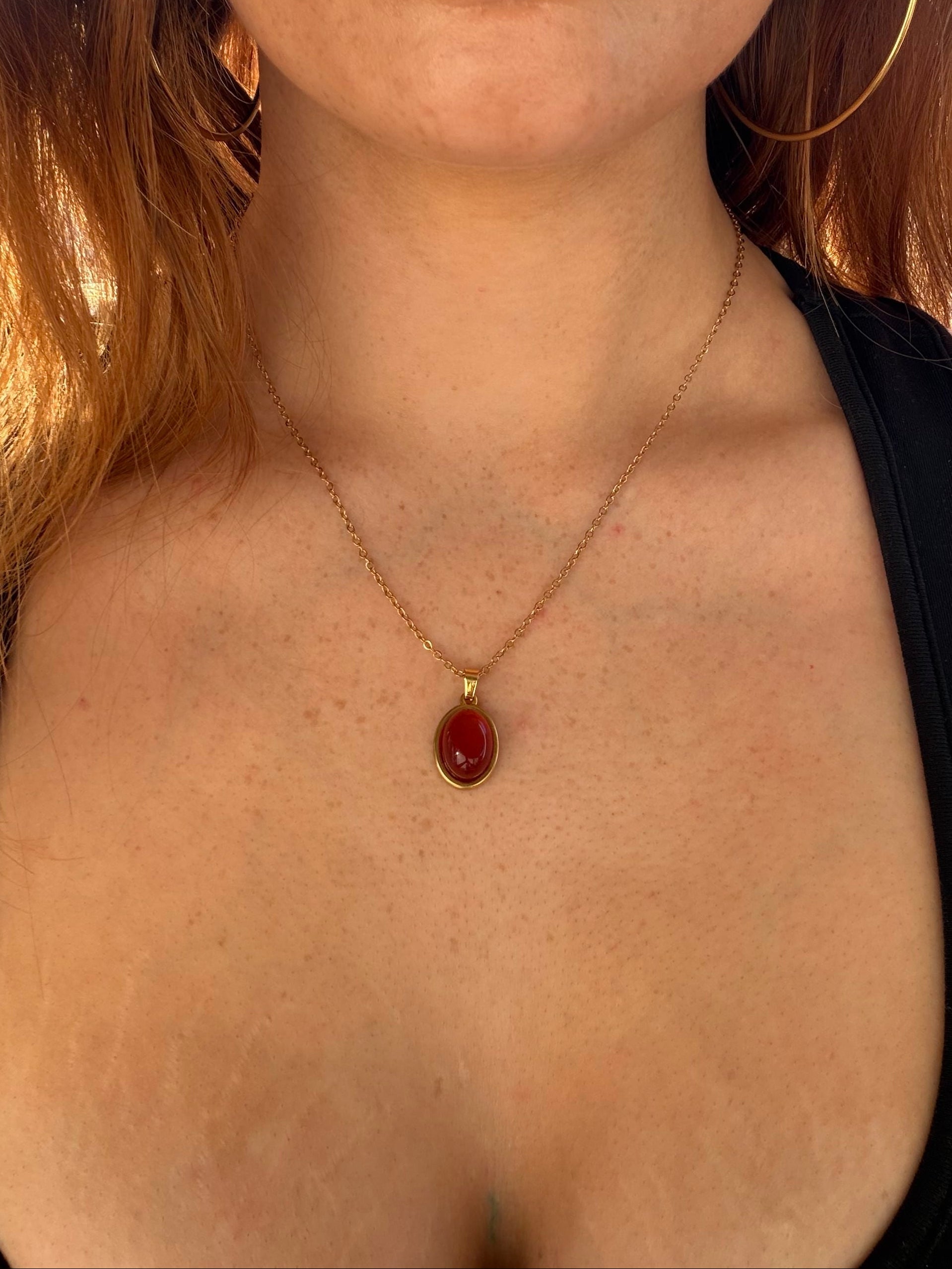 Close-up of a person wearing a gold necklace with a red pendant.
