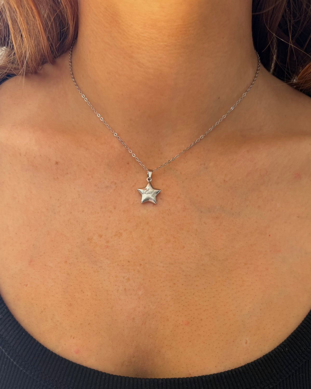 A close-up of a person's neck and chest wearing a delicate silver chain necklace with a small lucky star-shaped pendant.