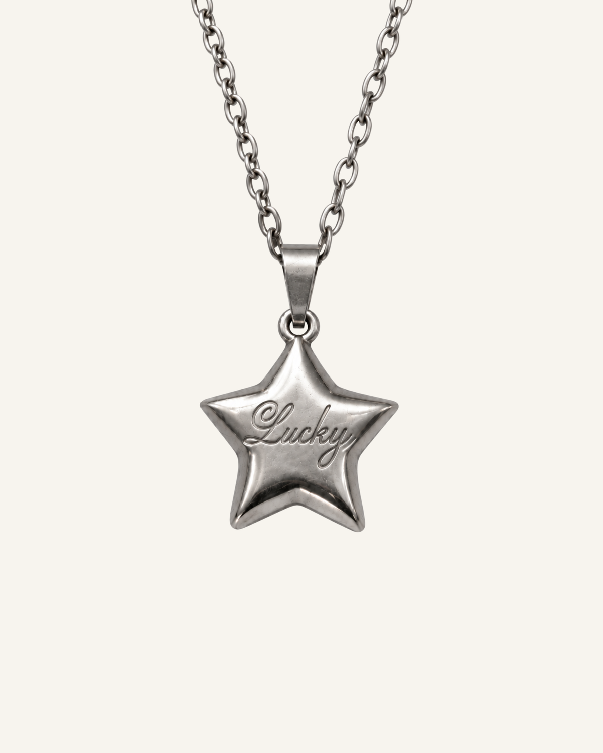 A silver star-shaped pendant necklace engraved with the word 'Lucky' in cursive, suspended from a matching silver chain against a light cream background.
