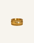 A textured gold ring with a raised central motif and beaded borders, centered on a plain off-white background.