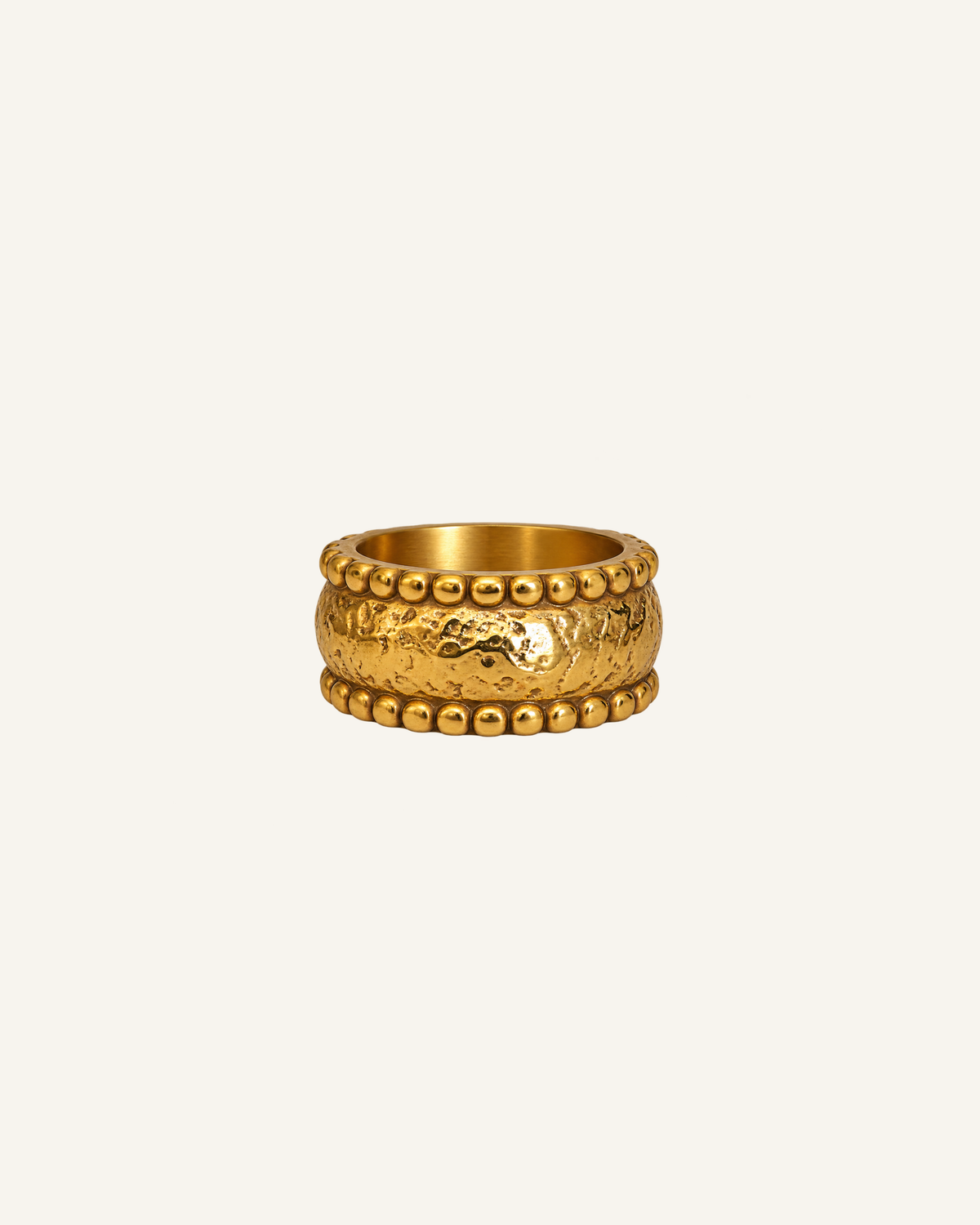 A textured gold ring with a raised central motif and beaded borders, centered on a plain off-white background.